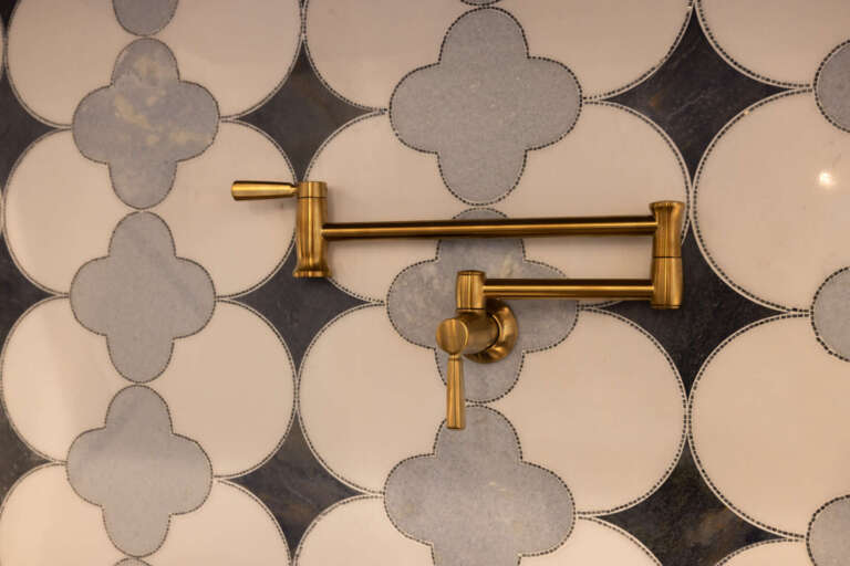 Close-up of brass articulating pot filler faucet against black and white geometric Moroccan quatrefoil mosaic tile backsplash in the kitchen of the Artful Haven luxury home renovation in Suwanee, GA by Infinite Home